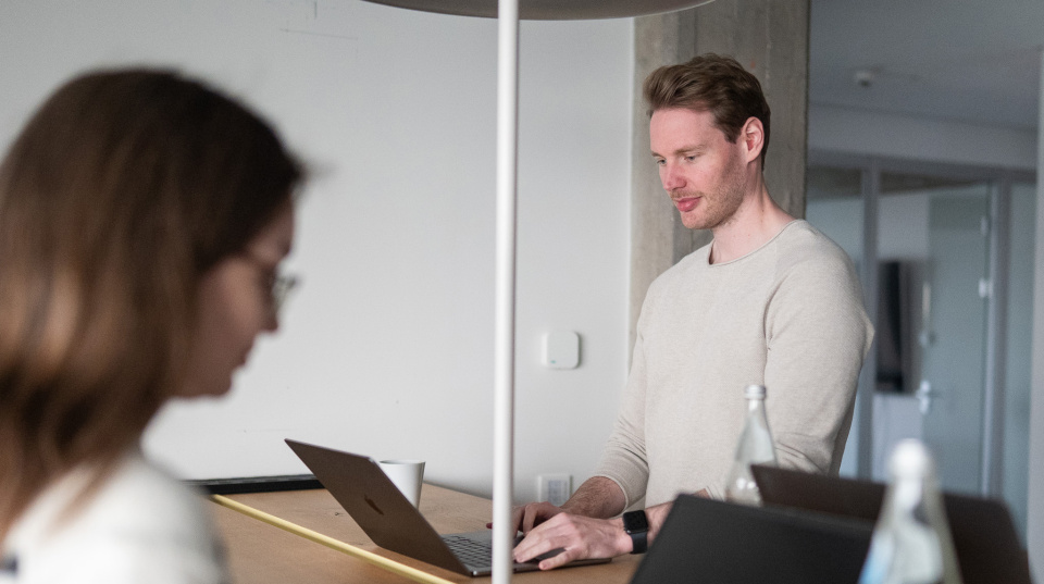 Zwei UEBERBIT Mitarbeiter an einem Stand-Up Tisch, die an ihren Laptops arbeiten.